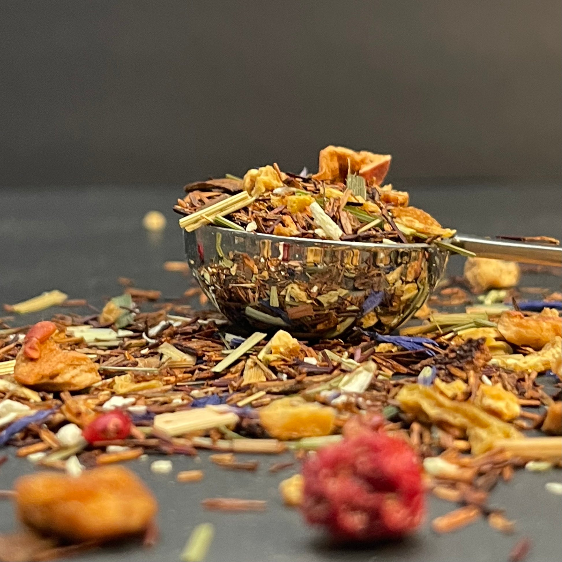 A moody, high-detail macro shot of Golden Compass loose leaf tea, highlighting the contrast between the vibrant dried citrus peel and the rich, earthy red of the organic Rooibos needles.