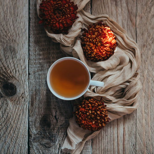 Cup of tea with pinecones and a scarf on a wooden surface