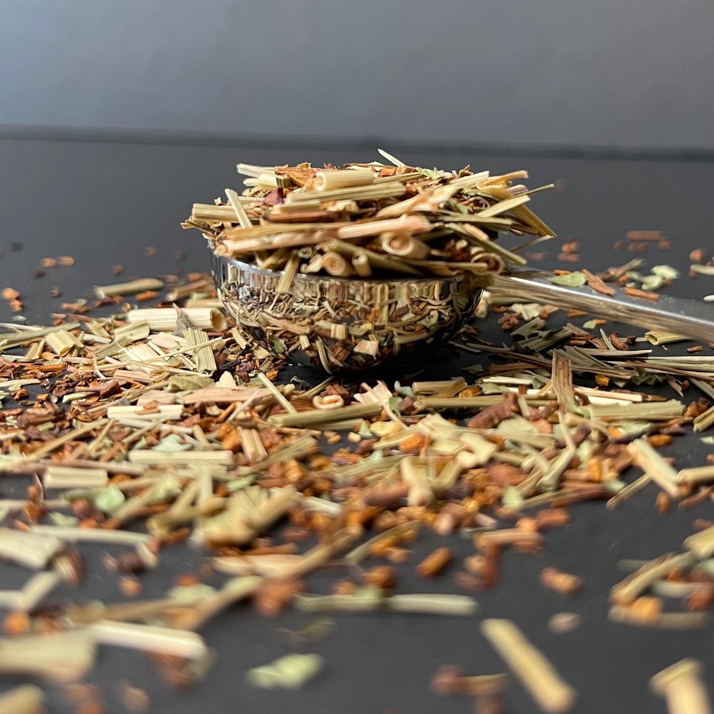 A vibrant close-up of Lemony Snicker loose leaf tea, showing the golden-red Rooibos needles accented by shards of dried ginger and bright green lemongrass stalks.