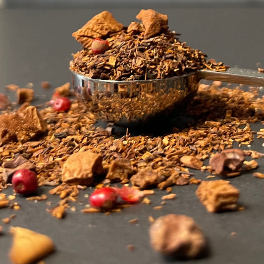 Monkey Business: Rich red Rooibos leaves blended with cocoa nibs and banana pieces, captured in a soft, moody light to highlight the botanical textures.